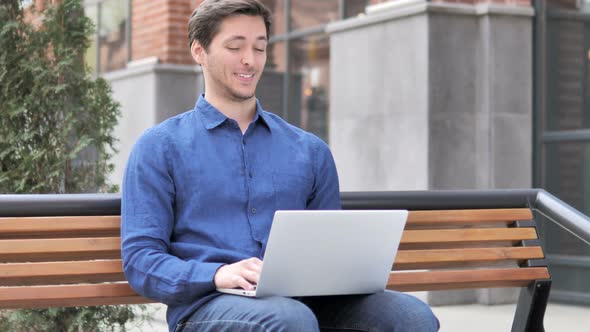 Online Video Chat on Laptop by Young Man Sitting on Bench