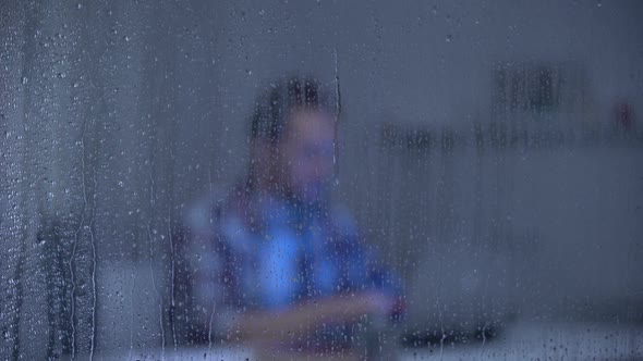 Tired Man Working on Laptop Late at Night Behind Rainy Window, Freelance
