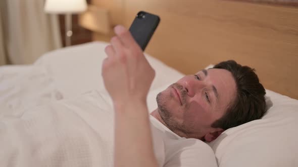 Middle Aged Man using Smartphone while Sleeping in Bed