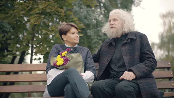 Positive Handsome Senior Man Talking with Woman Sitting on Bench in Autumn Park