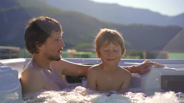 A Young Man and His Son Relaxing in the Hot Tub on a Rooftop with a View on Mountains