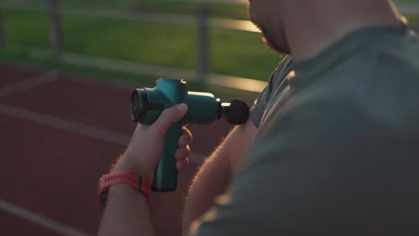 An Athlete Massages with a Percussion Therapy Gun to Relieve the Pain of Muscle Aches After a