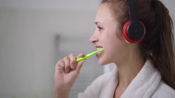 Side View Face of Concentrated Slim Beautiful Young Woman in Headphones Brushing Teeth in Slow