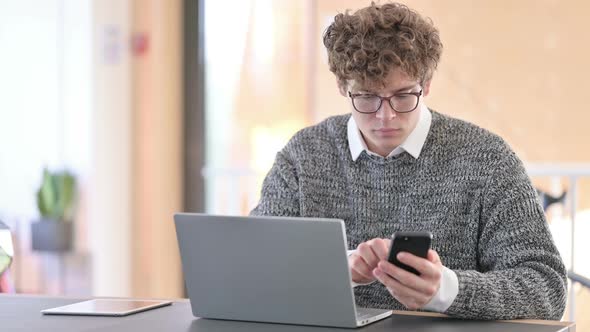 Young Man Using Smartphone and Laptop at Work