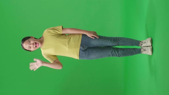 The happy young Asian man waving hand while standing on green screen in the studio