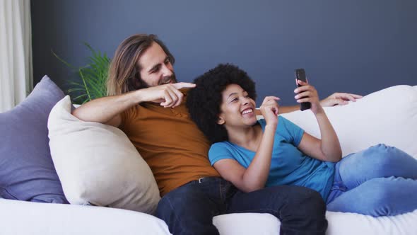 Mixed race couple having a videocall on smartphone on the couch at home