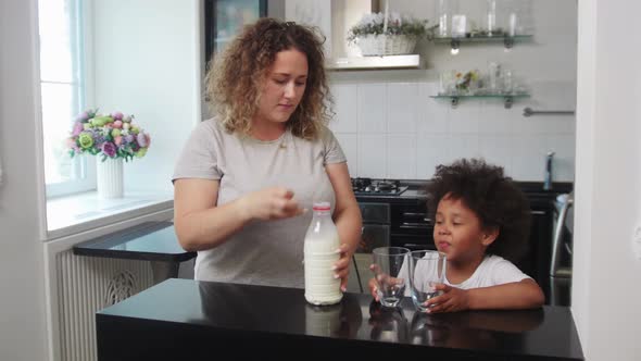 White Mother and Her Mixed Black Daughter at the Kitchen  the Woman Pouring Milk in Glasses