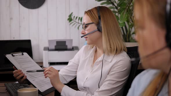 Woman with Headset in the Office at a Computer Desk She Looks Through Documents