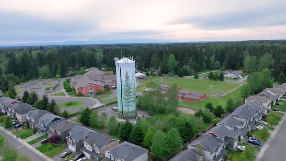 Orbiting aerial shot around a suburban water tower with an elementary school in the background.