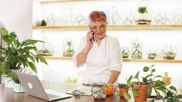 Senior Caucasian Florist Wearing Eyeglasses in Workplace Talking on Mobile Phone