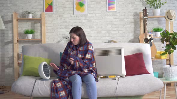 Frozen Young Woman in the Living Room and Basking Next To Electric Heaters