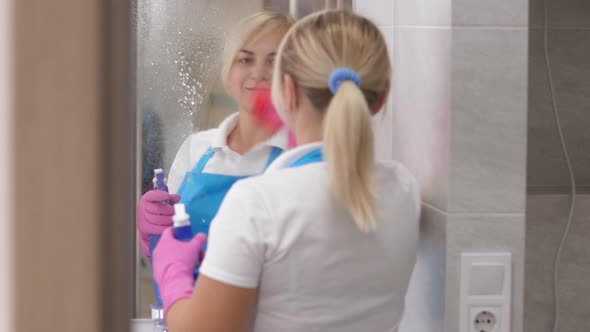 Smiling Woman Cleaner Wiping Mirror in Bathroom