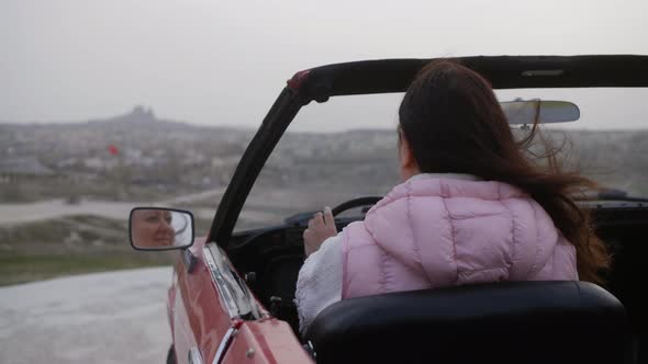 Woman is Sitting in Her Red Retro Cabriolet Looking at Mirror Rear View