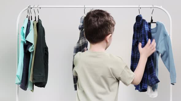 Boy preschooler standing by the hangers, racks up clothes, and chooses clothes for today.