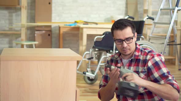 Portrait of a Young Disabled Man Next To a Wheelchair Collects a Bedside Table