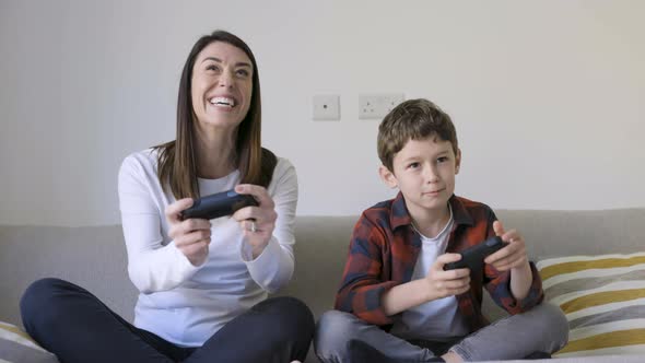 Mother and son playing with gaming consoles sitting on couch