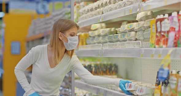 Young Woman in a Medical Mask Picks Eggs in the Supermarket