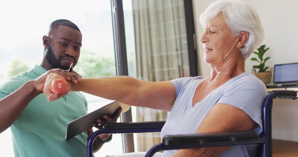 Video of happy african american male physiotherapist exercising with caucasian senior woman