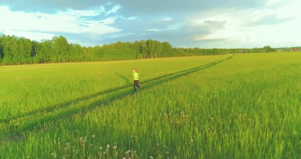 Sporty Child Runs Through a Green Wheat Field. Evening Sport Training Exercises at Rural Meadow