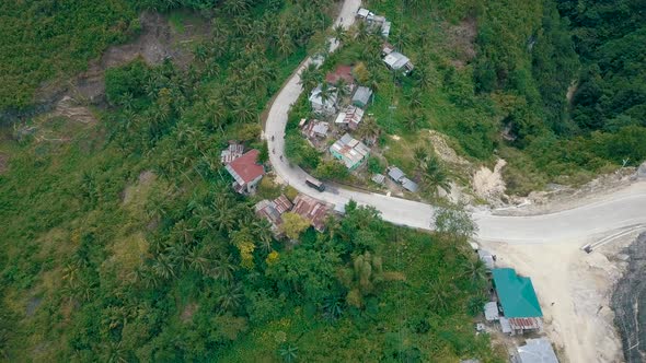 Aerial camera tilts down as it flies over a road on a mountainside in Cebu as vehicles drive down th