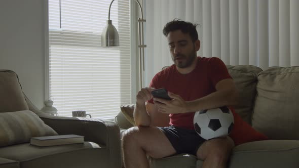 Soccer Fan Checking Social Media While Holding Soccer Ball at Home