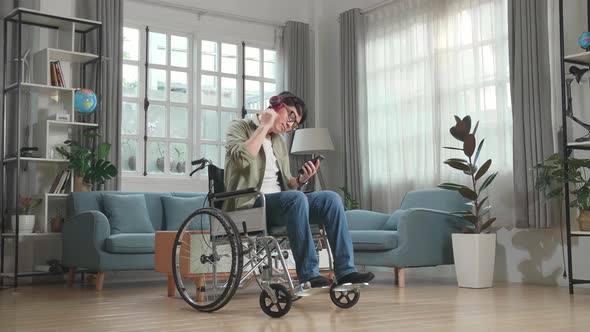 Asian Man Sitting In A Wheelchair Listening To Music With Headphones And Dancing In Living Room
