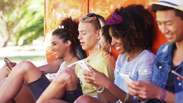 Friends using mobile phone near camper van in park 4k