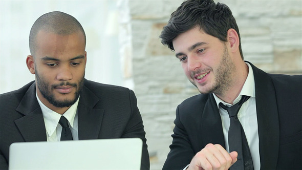 Two Young Men Discussing Information On The Laptop