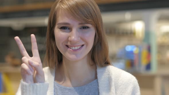 Portrait of Young Woman Gesturing Victory Sign in Cafe