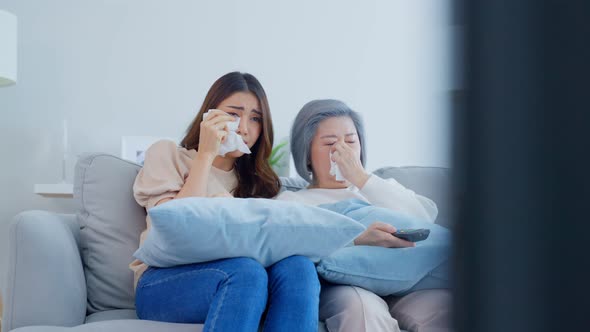 Asian senior mature woman and daughter sitting on sofa watch sad movie.