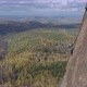 Aerial View of a Man Climbing a Rope To the Top of a Mountain Overlooking the Autumn Forest - VideoHive Item for Sale