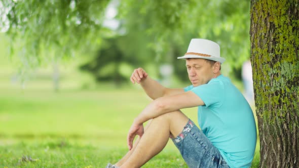 Lonely Man Resting in the Shade of a Tree While Sitting in the Park Side View