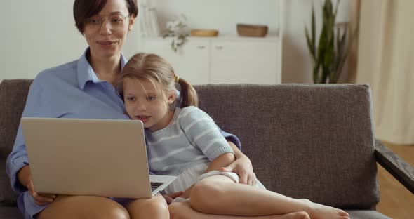 Caucasian Mom with Cute Daughter Sitting on Comfortable Sofa in Living Room at Home Hugging Watching