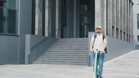 Man Courier Food Delivery with Yellow Thermal Backpack Rides the Street on an