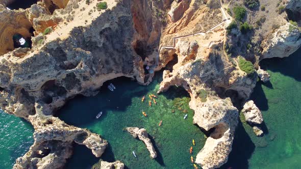 Drone shot of kayaks and boats passing in the ocean, people exploring caves and tunnels.