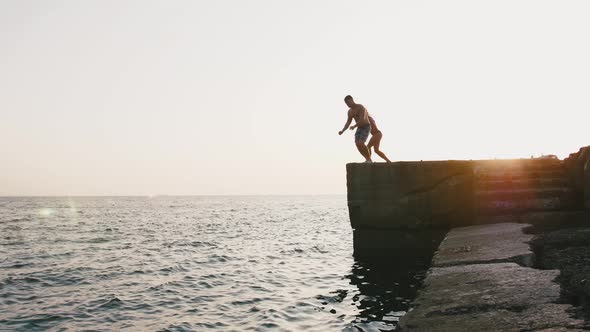 Young Woman and Man Jumping From a Pier Into the Sea and Doing Tricks During Beautiful Sunrise Slow