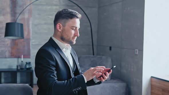 Successful Happy Businessman in a Luxurious Black Suit Sends Text Messages on His Modern Smartphone