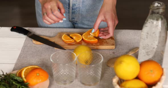 Female hand cut orange and put in glasses, making lemonade