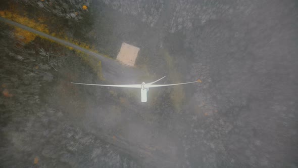 Static Top View Drone Shot of Working Windmill Turbine in Green Forest Covered By Cloud Mist