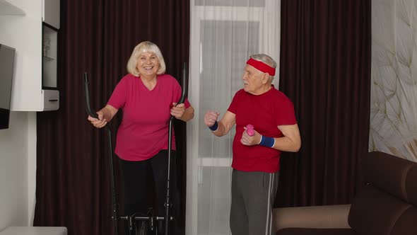 Old Senior Couple Exercising on Orbitrek Doing Weight Lifting Sport Dumbbells Exercises at Home