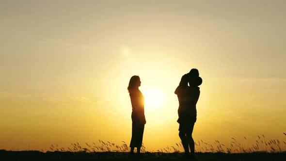 Silhouette of a Happy Family Against a Bright Sunset. Father and Mother Kiss and Hug Their Son.