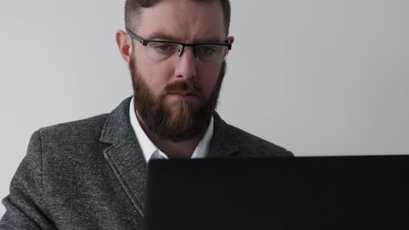 Close up view of bearded middle aged man in glasses using laptop computer on the white background