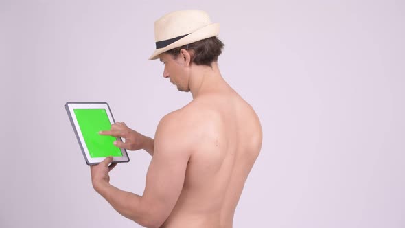 Rear View of Muscular Tourist Man Using Digital Tablet Shirtless