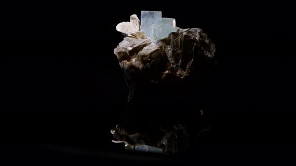 An aquamarine crystal emerging from the matrix of muscovite turns slowly with a reflection of the sa