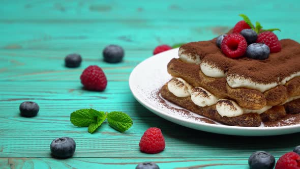 Portion of Classic Tiramisu Dessert with Raspberries and Blueberries on Wooden Background