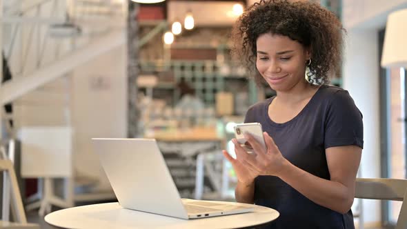 Smartphone Use By Young African Woman with Laptop in Cafe