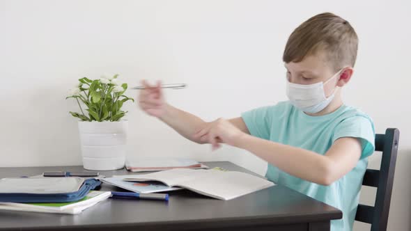 A Young Boy in a Face Mask Does Homework for School and Dances at a Table at Home