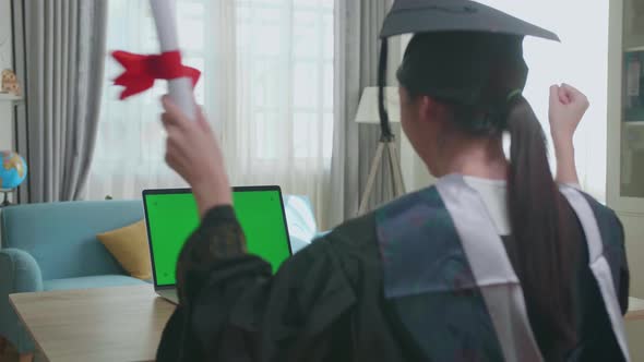 Asian Woman Celebrating On Laptop Computer With Green Mock-Up Screen During An Online Video Call