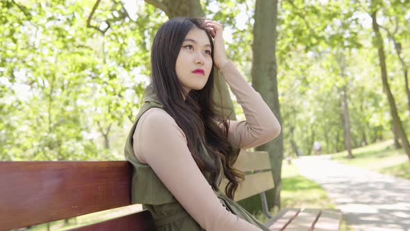 Young Asian Woman Thinks About Something As She Sits Bench Park Sunny Day