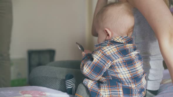 Cute Boy in Warm Clothes Plays with Spoon By Mommy on Bed